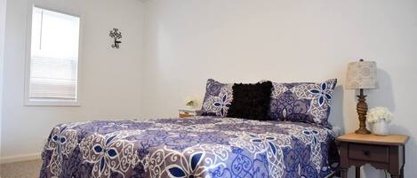 A bedroom with a bed, a nightstand, a lamp, and a window.