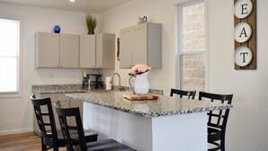 Una cocina con encimera de granito, armarios blancos y una isla central con sillas.