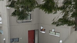 A snow-covered outdoor area with a red door, a small window, and a wooden staircase leading up.