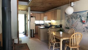 A cozy kitchen with wooden cabinets, a dining table with chairs, a map on the wall, and a black stove.