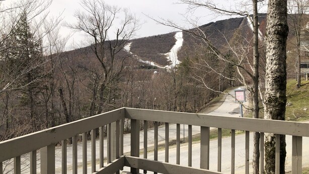 A wooden deck with a metal railing overlooking a road and a mountain.