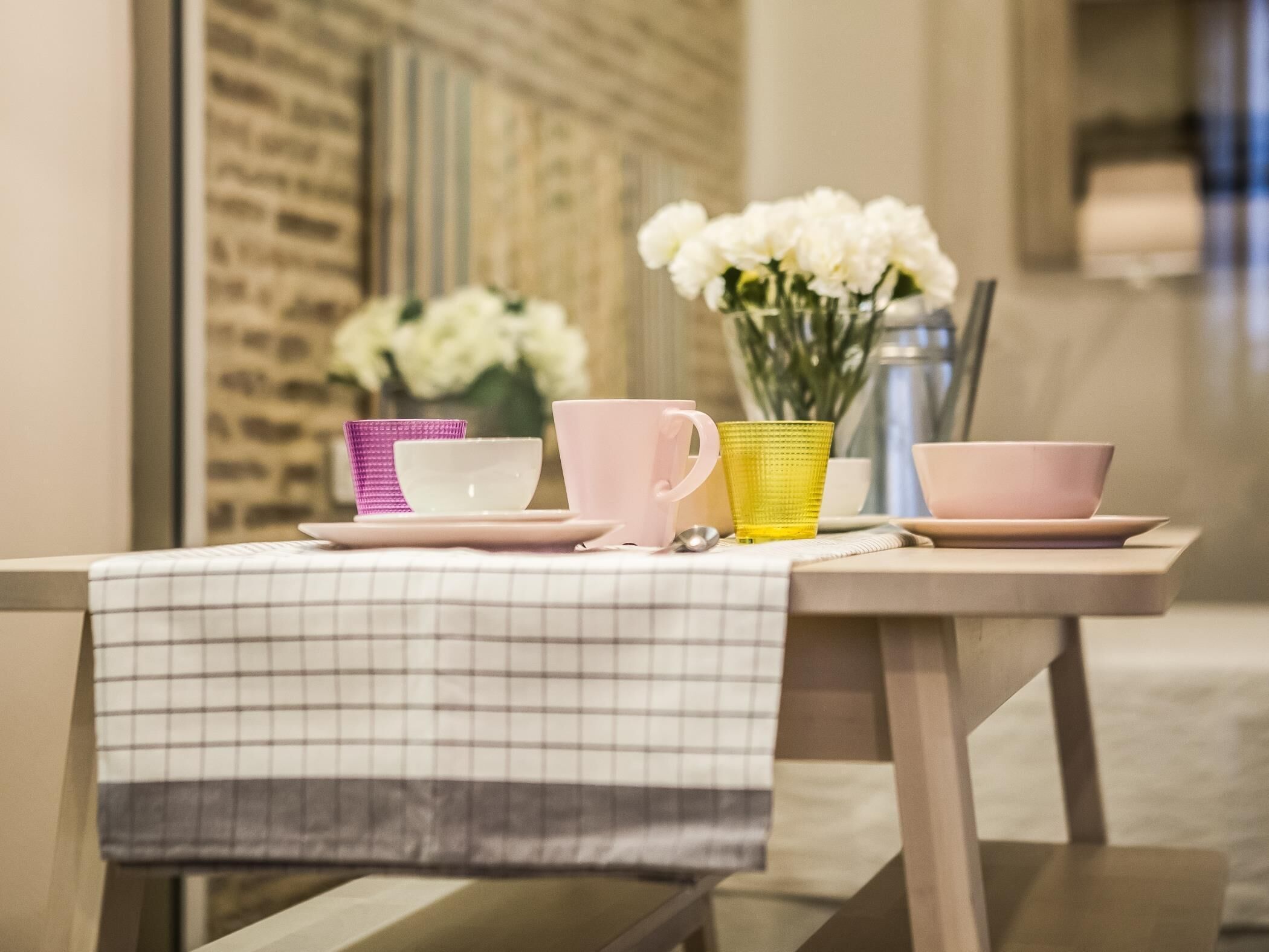 A table with a checkered tablecloth, a vase of white flowers, and a metal kettle.
