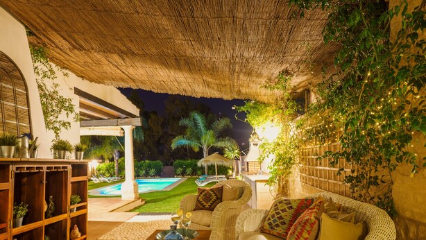 An outdoor patio area with wicker furniture, a pool, and potted plants.