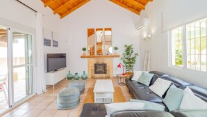 A spacious living room with a high wooden ceiling, a fireplace, a television, and a large window.