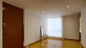 A room with a brown door, a mirror on a small table, a window with white curtains, and a tiled floor. - ❤️Lima AIRPORT❤️ 4 min AWAY I 3 BDR I Smartlocks (Callao)