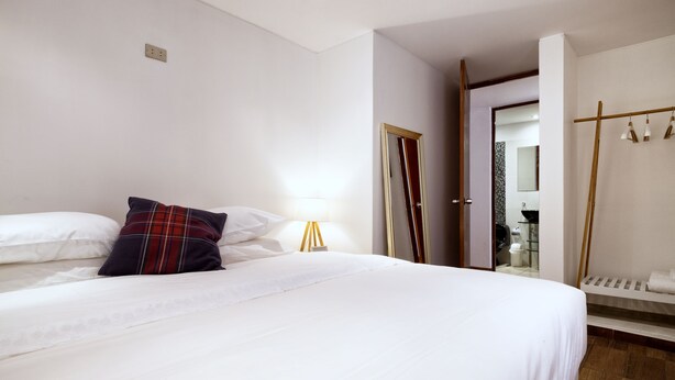 A hotel room with a large bed, a bedside table with a lamp, a wardrobe, and a mirror. - ❤️Lima AIRPORT❤️ 4 min AWAY I 3 BDR I Smartlocks (Callao)