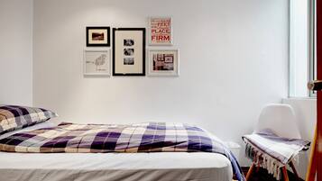 A bedroom with a bed, a chair, and wall art.