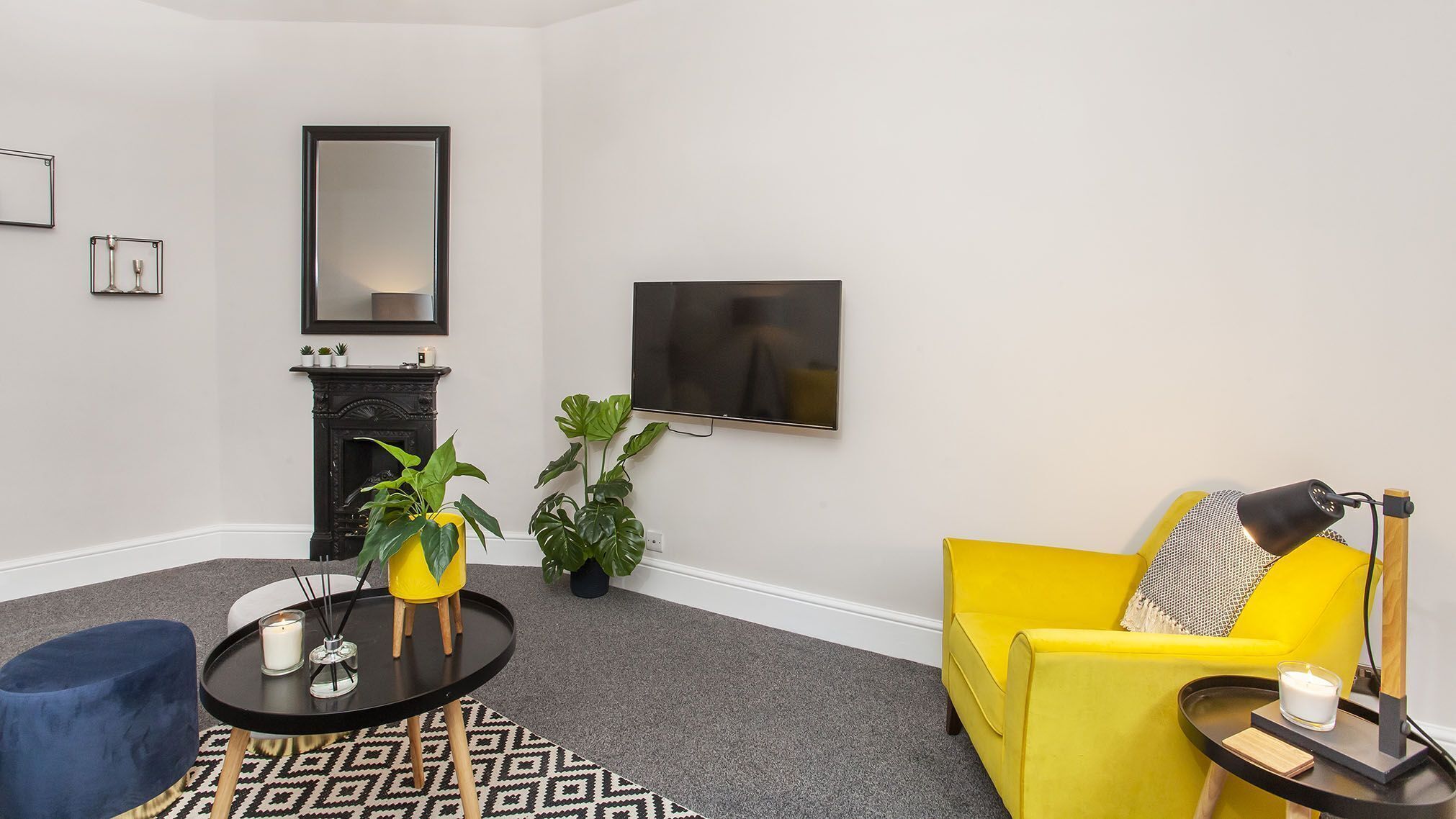 A modern living room with a yellow sofa, a blue armchair, a round black coffee table, and a fireplace.