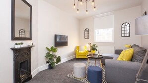 A living room with a fireplace, a yellow armchair, a grey sofa, and a TV mounted on the wall. - Sleeps 6 guests  in 2 bedrooms (York)