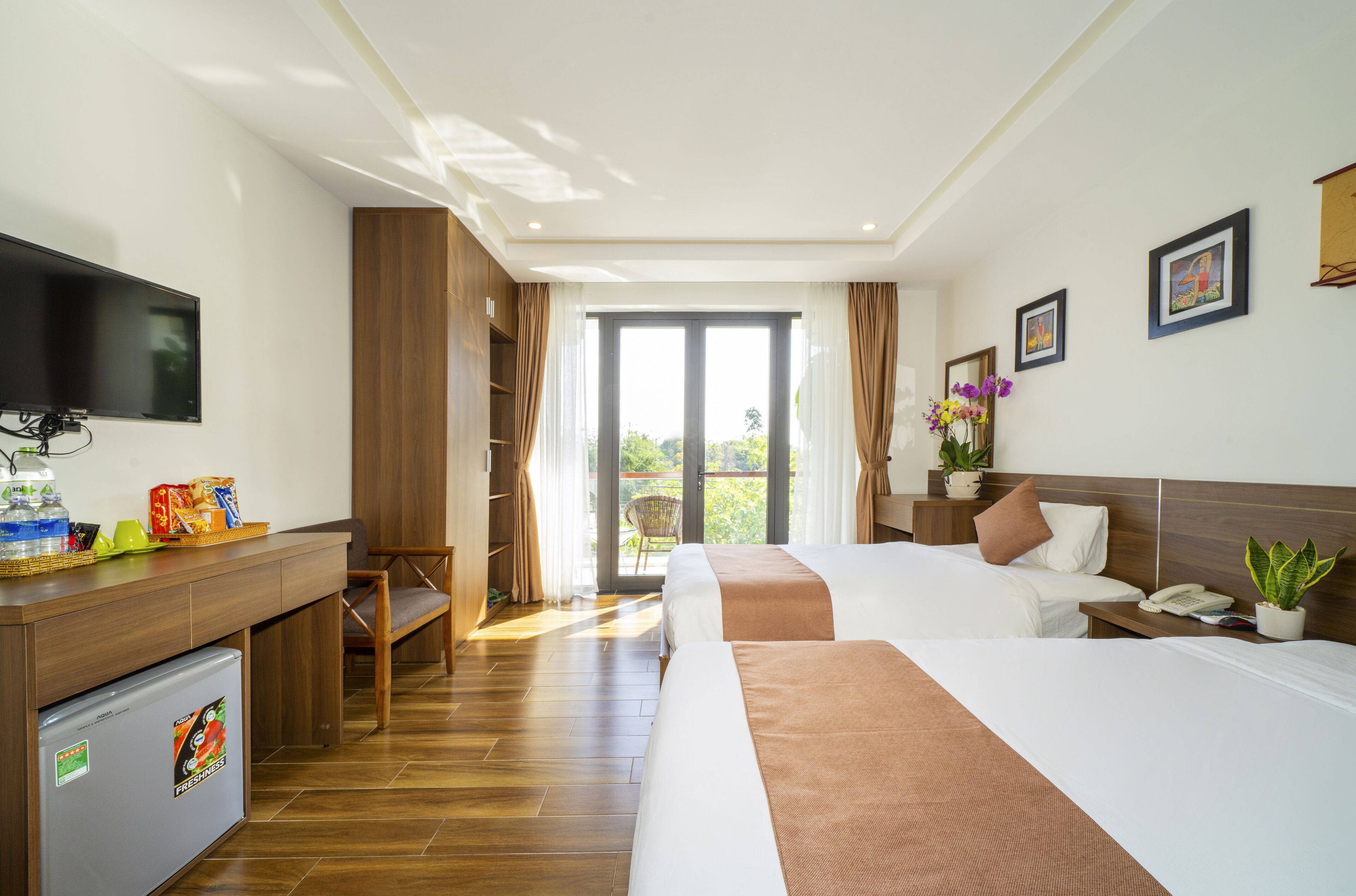 Quarto de hotel com duas camas, uma escrivaninha com televisão, um refrigerador e vista para o exterior.