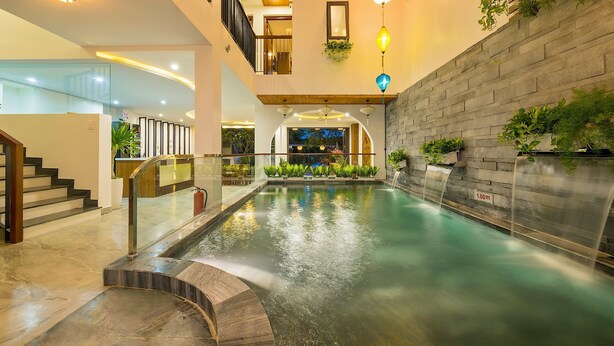 A modern indoor pool area with a stone wall, glass railings, and multiple levels. - Brother Villa Hoi An (Da Nang)