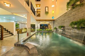 A modern indoor pool area with a stone wall, glass railings, and multiple levels. - Brother Villa Hoi An (Da Nang)