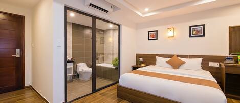 A modern hotel room with a large bed, a glass shower enclosure, and a wooden floor.