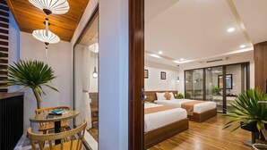 A hotel room with a wooden floor, two beds, a dining area with a table and chairs, and potted plants. - Brother Villa Hoi An (Da Nang)