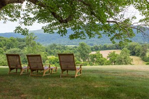 A grassy outdoor area with three wooden chairs under a tree, overlooking a hilly landscape. - Ramsay Estate Cottage – Historic Vineyard Retreat with Mountain Views (Greenwood)