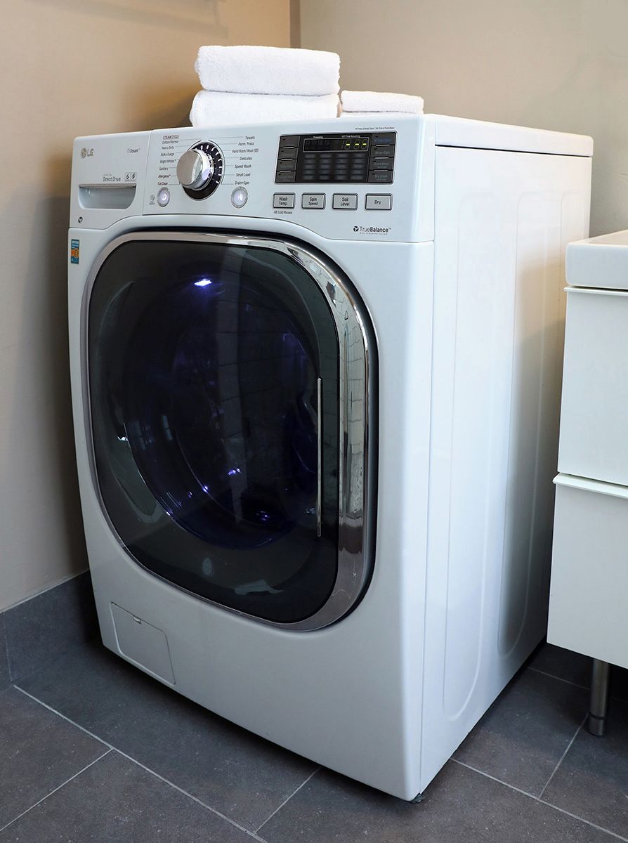 A front-loading white washing machine with a control panel, a transparent door, and a white towel on top.