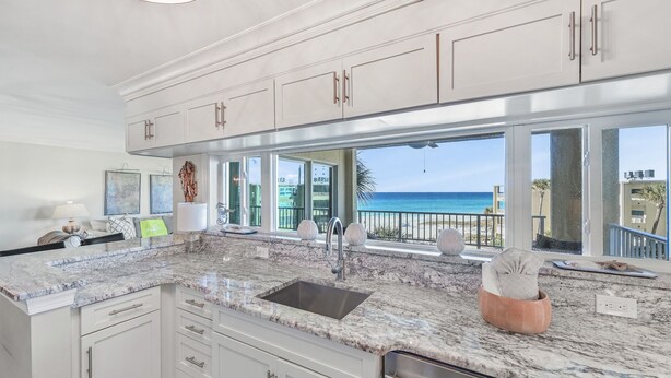 A kitchen with white cabinets, a marble countertop, and a view of the ocean. - Beach-side, beautiful low-rise with uncrowded beach! (Destin)