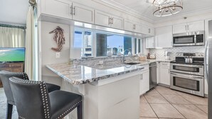A modern kitchen with white cabinetry, a granite countertop, stainless steel appliances, and a large window offering a city view. - Beach-side, beautiful low-rise with uncrowded beach! (Destin)