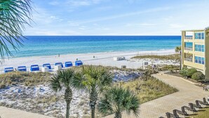 A beach view with a building, palm trees, and beach chairs. - Beach-side, beautiful low-rise with uncrowded beach! (Destin)