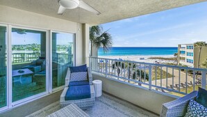 A balcony with a ceiling fan, a glass door leading to an outdoor seating area, and a view of the beach. - Beach-side, beautiful low-rise with uncrowded beach! (Destin)