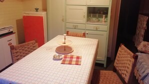 Une petite pièce comprenant un coin cuisine, un lit recouvert d’une couverture à carreaux et une chaise en osier.