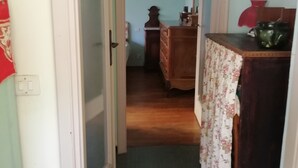 Un couloir étroit avec une commode en bois et une lampe rouge posée sur une table.