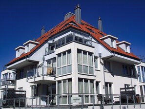 A white building with a red roof, multiple balconies, and large windows.