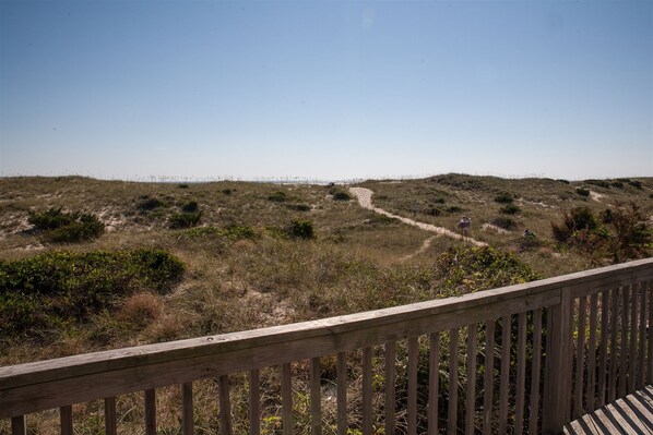 A wooden deck overlooking a sandy landscape with sparse vegetation and a clear sky.