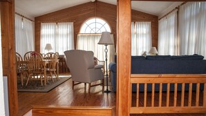 A cozy room with a wooden ceiling, a dining table with chairs, a sofa, and a lamp.