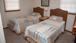 A room with two single beds, each with a wooden headboard, a bedside table with a lamp, and a framed picture on the wall.