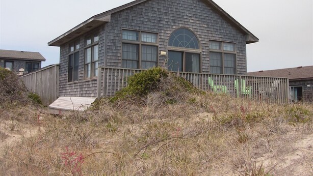 A two-story building with a sloped roof, large windows, and a wooden deck.