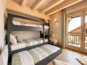 A bunk bed with three levels, a teddy bear on a chair, and a wooden balcony.
