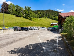 A parking area with vehicles, a building with a red roof, and a green vehicle in the distance. - Luxury chalet for 10 with sauna in village center, WiFi included (Notre-Dame-de-Bellecombe)