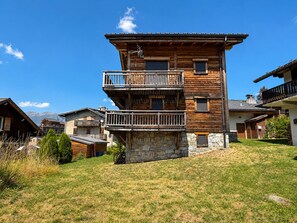A multi-story wooden building with balconies, stone foundation, and a clear sky. - Luxury chalet for 10 with sauna in village center, WiFi included (Notre-Dame-de-Bellecombe)