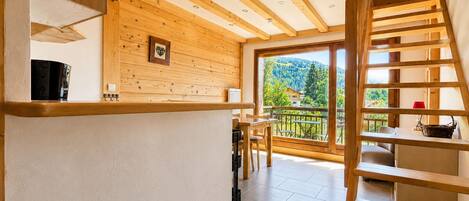 A wooden interior with a staircase leading to a balcony overlooking a mountainous landscape.