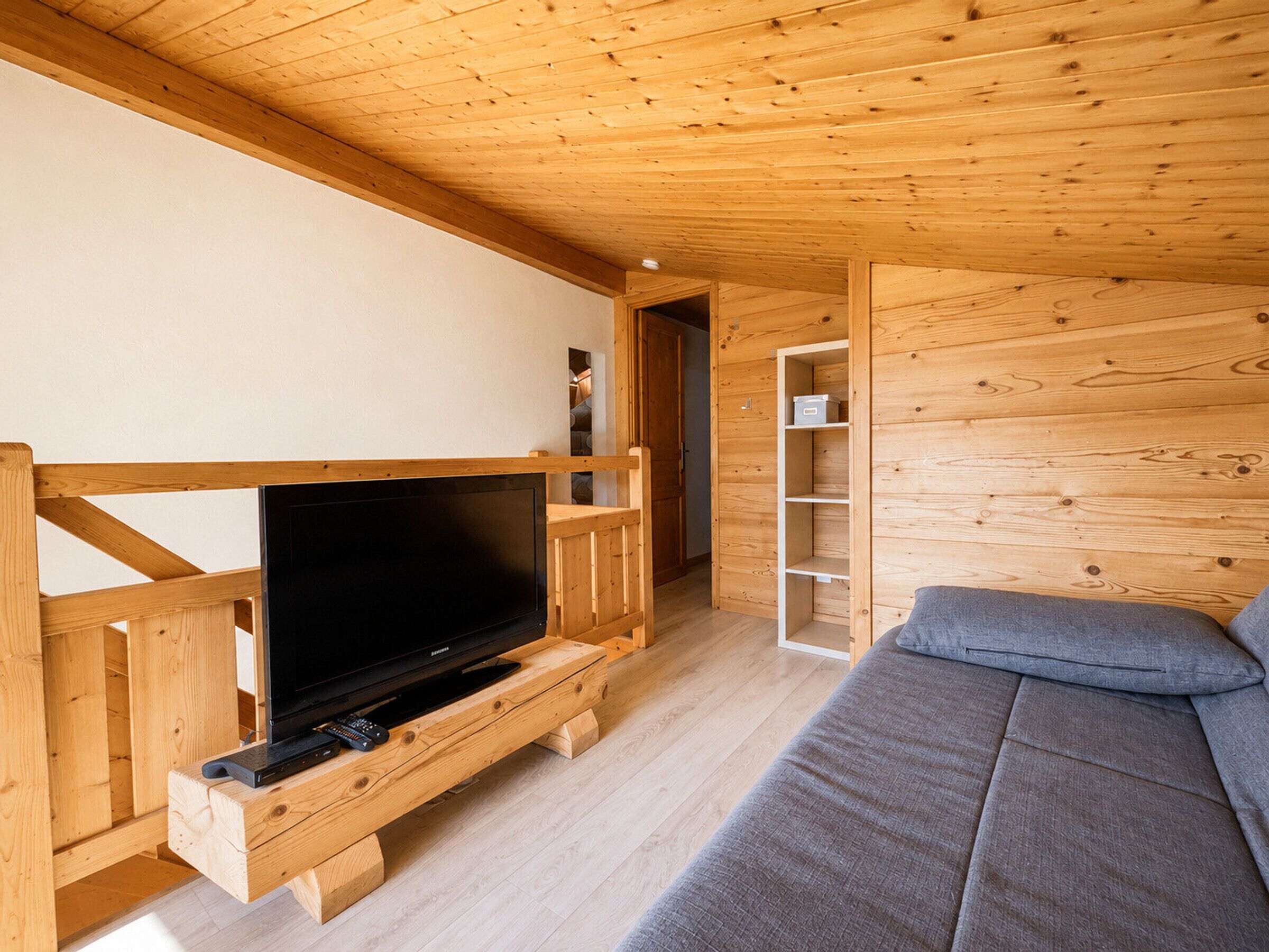 Un interior de madera con una televisión sobre un mueble de madera, un sofá y una estantería de madera.