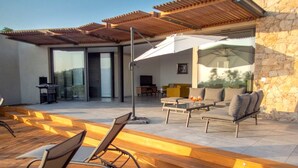 Een modern terras buiten met houten vloeren, een overdekte zithoek en een stenen muur.
