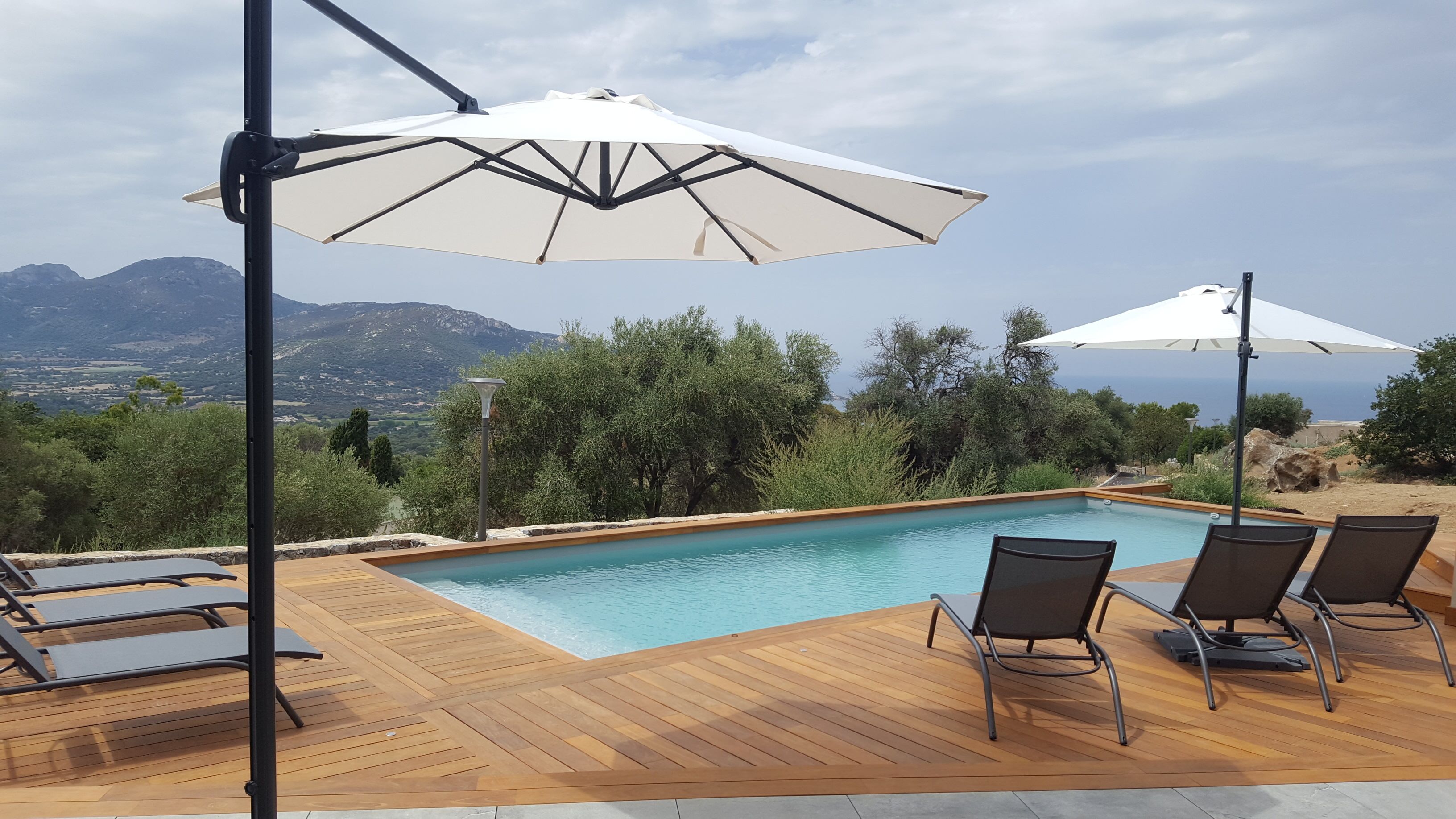 Area piscina con pavimento in legno, poltrone relax e ombrelloni.