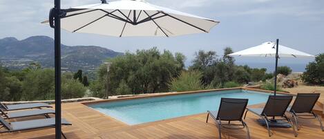 Area piscina con pavimento in legno, poltrone relax e ombrelloni.