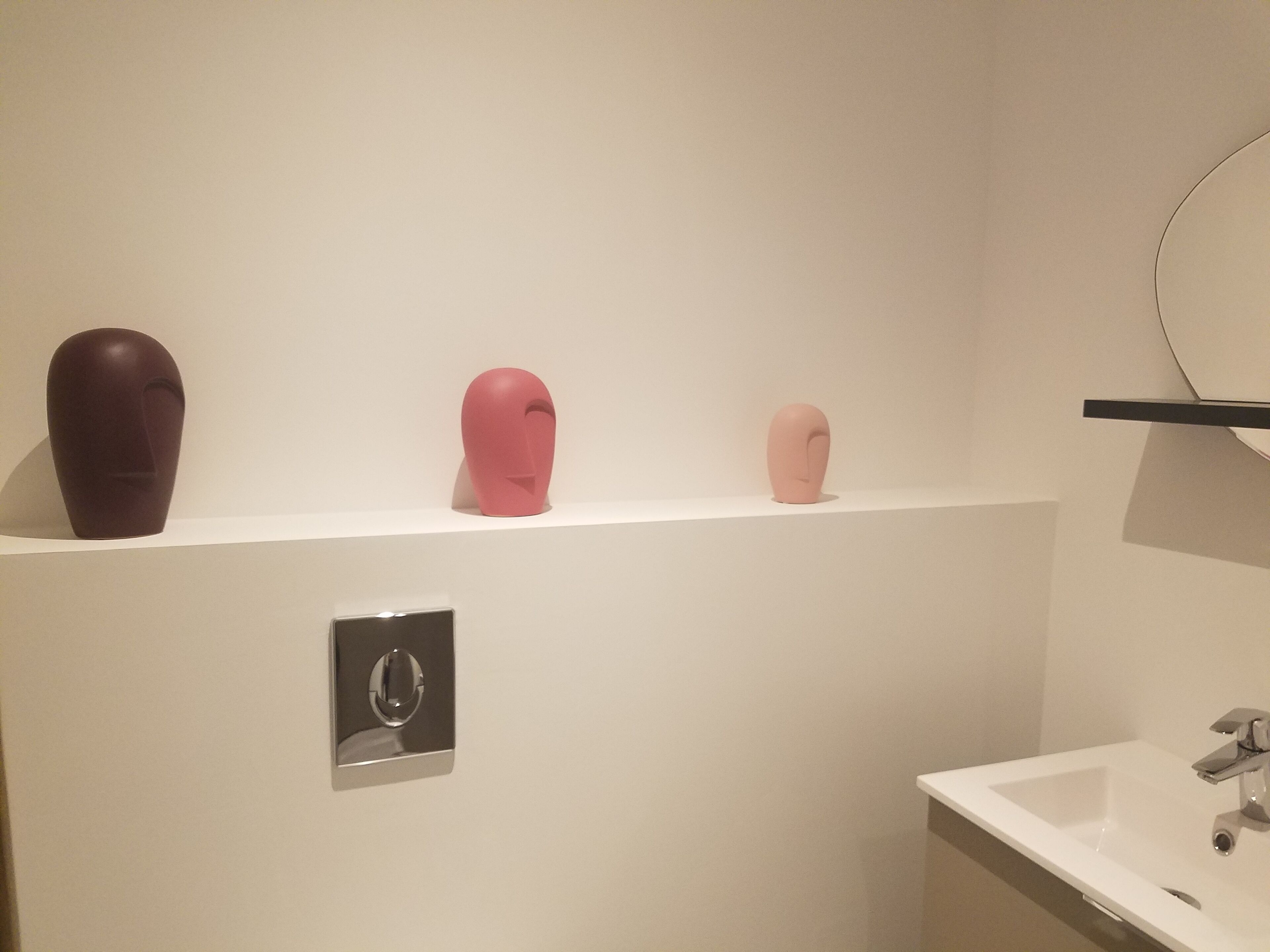 Un baño con un lavamanos blanco, un espejo y tres esculturas abstractas en un estante.