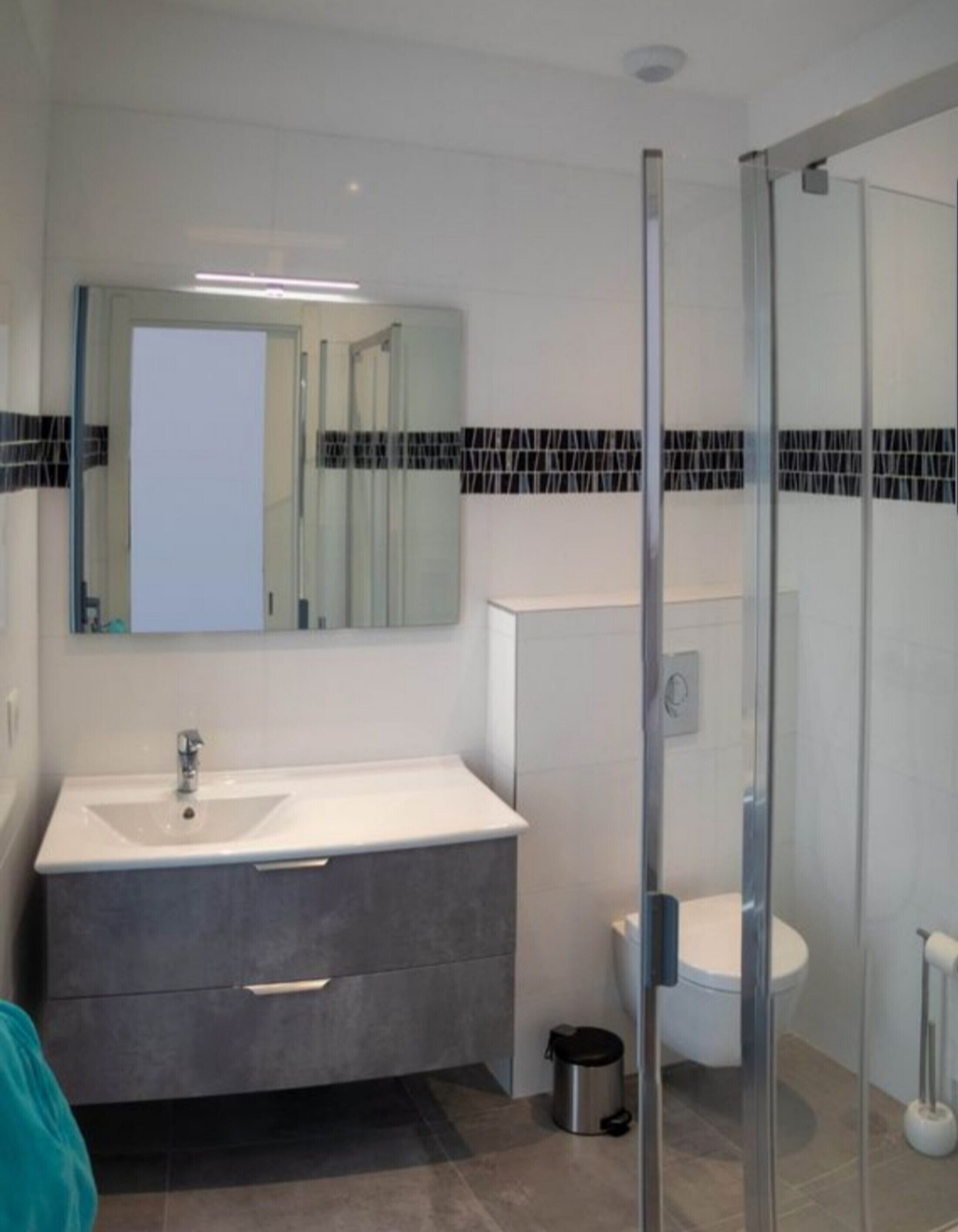 Un baño moderno con cabina de ducha de vidrio, un lavabo blanco y encimera oscura, y un inodoro.