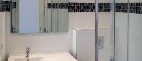 Un baño moderno con cabina de ducha de vidrio, un lavabo blanco y encimera oscura, y un inodoro.