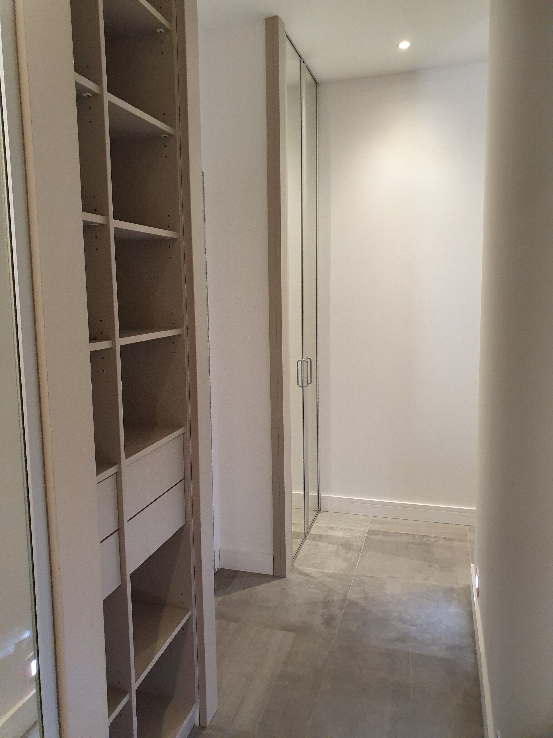 A hallway with a built-in closet featuring multiple shelves and a sliding door closet.