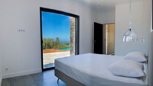 Een moderne slaapkamer met een groot bed, uitzicht op het strand en een schuifdeur.
