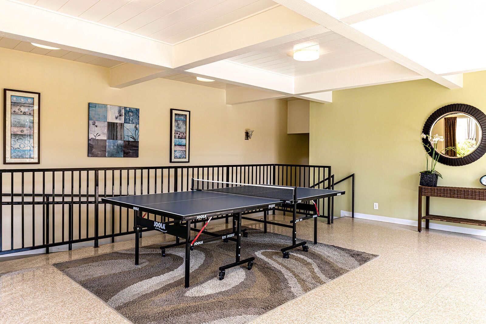 Une table de ping-pong dans une pièce au plafond haut, des œuvres d’art aux murs et une console sur laquelle sont posés un miroir et une plante.