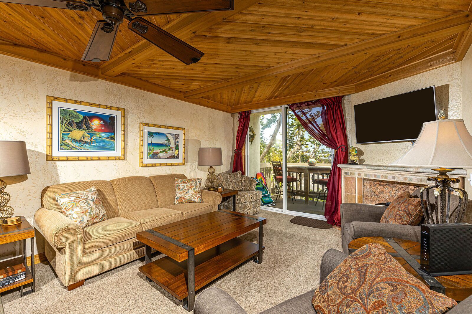 A cozy living room with a wooden ceiling, a fireplace, a television, and two framed pictures on the wall.