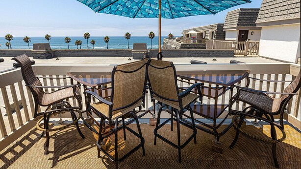 Une terrasse avec une table et des chaises, un parasol et une vue sur l’océan.
