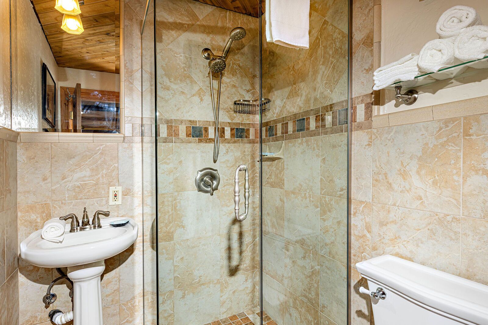A bathroom with a glass-enclosed shower, a pedestal sink, and a toilet.
