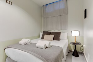 A hotel room with a bed, pillows, a bedside lamp, and a window with curtains.