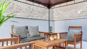 Ein Holz-Sitzbereich im Freien mit zwei Stühlen, einem Tisch, einer Topfpflanze und einer Laterne.